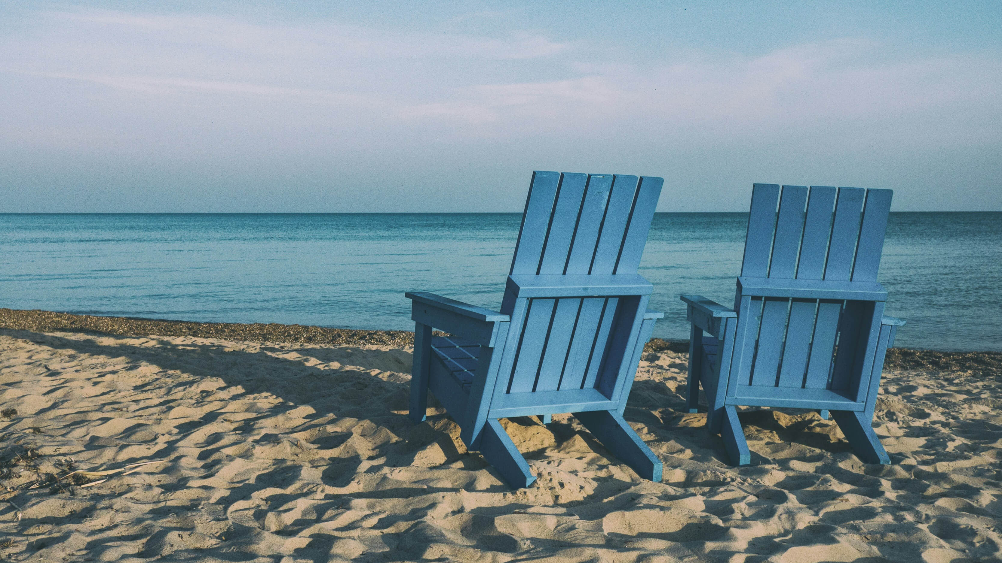 Zwei Holzstühle stehen am Strand - Blick auf das Meer